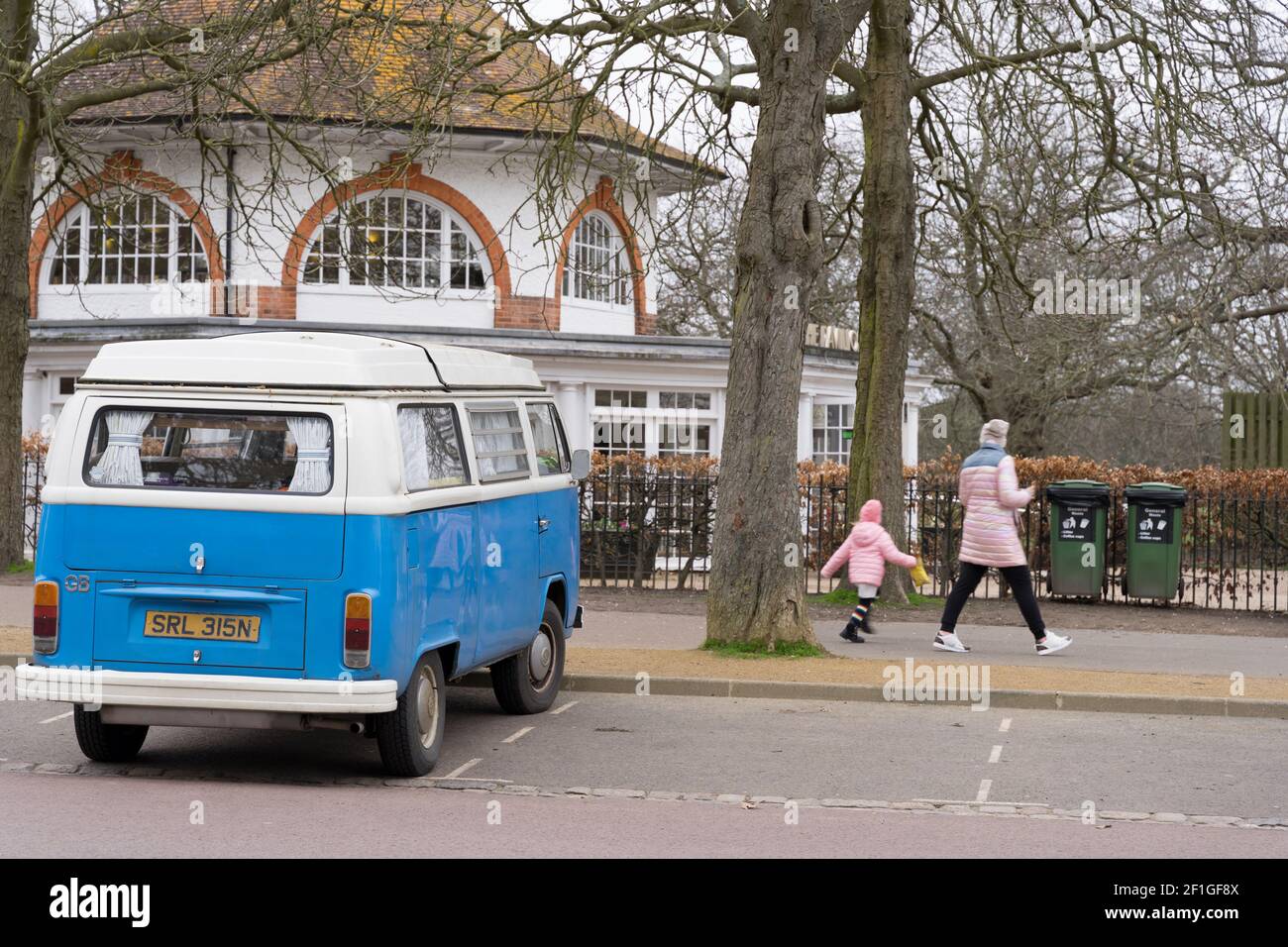 womanna and young girl walks past VOLKSWAGEN MOTOR CARAVAN in blue and white parked  in London greenwich park Stock Photo