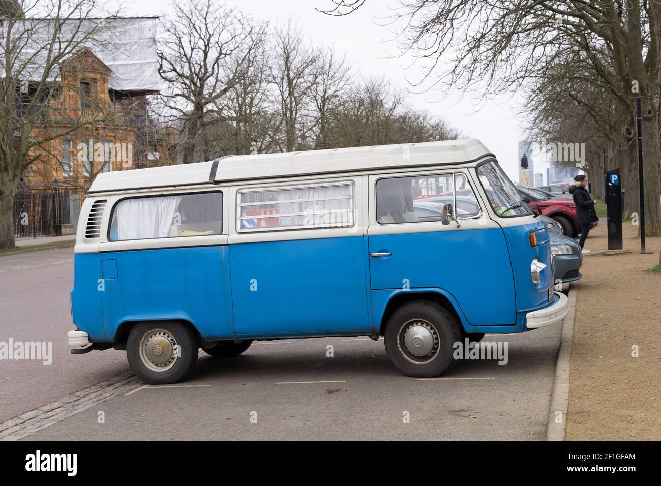 VOLKSWAGEN MOTOR CARAVAN in blue and white parked  in London greenwich park while its owner buys parking ticket from parking machine Stock Photo