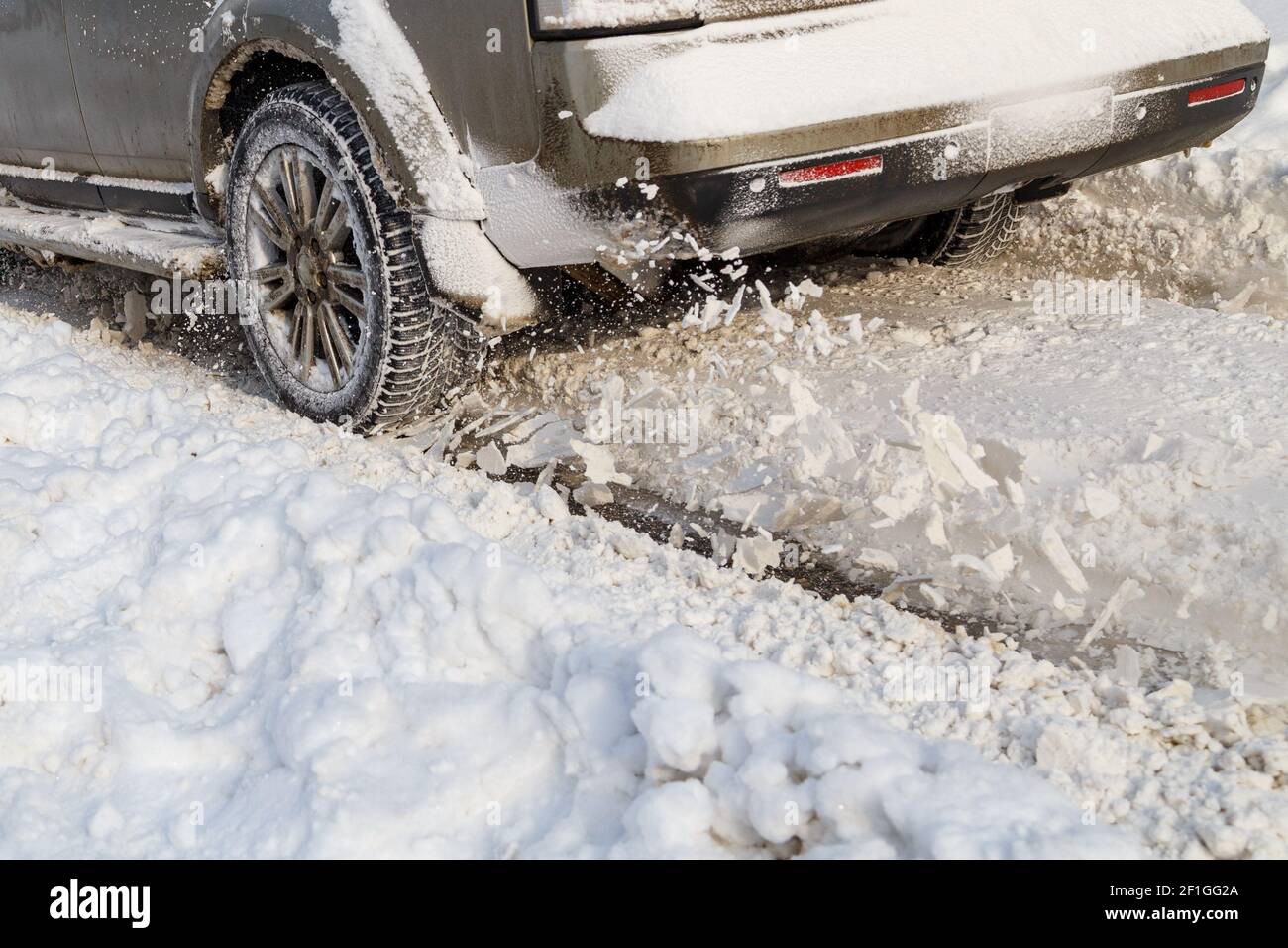 Road snow flies up from a vehicle's spinning wheel. Car's wheels spin