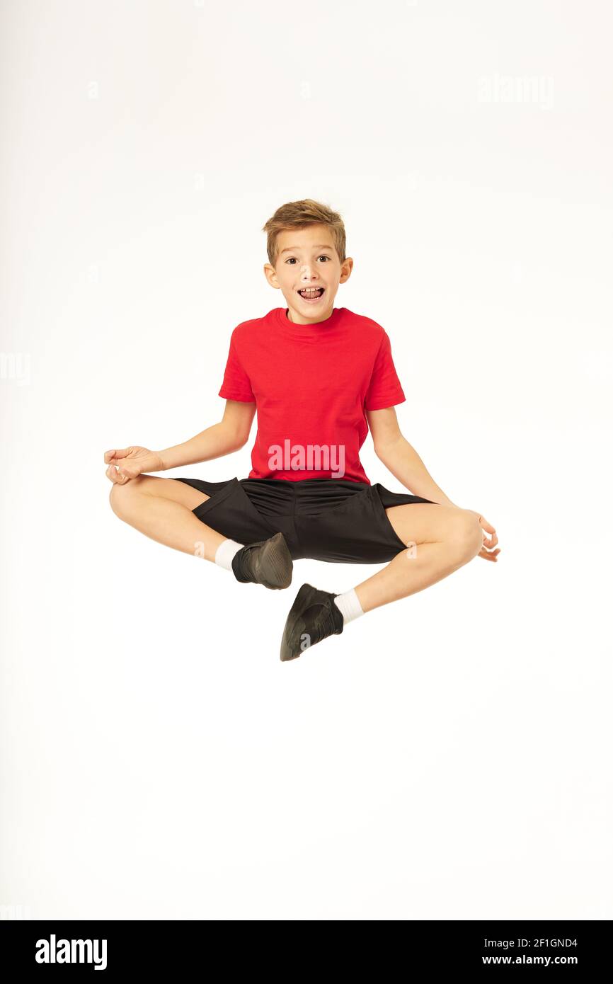 Adorable male kid looking at camera and smiling while doing lotus pose in the air. Isolated on white background Stock Photo