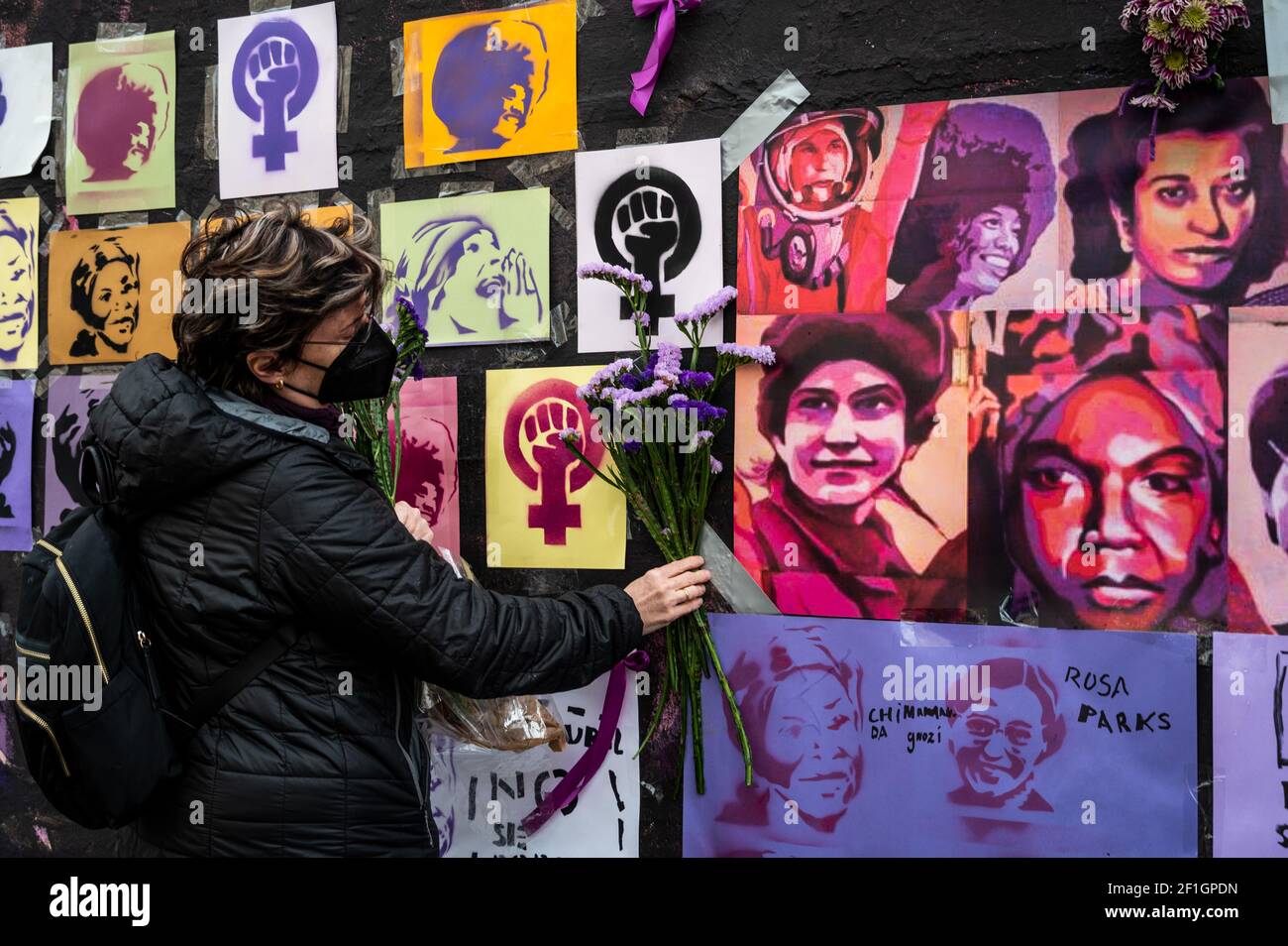 Madrid, Spain. 8th March, 2021. A woman placing flowers in a feminist mural that appeared today vandalized during International Women's Day. Placards of women have been placed over the paintings after the mural was vandalized with black paint. The mural represents famous women from around the world, with the faces of 15 women who are part of history for their fight in favor of equality: Angela Davis, Frida Kahlo, Nina Simone, Rigoberta Menchu, Lucia Sanchez Saornil, Rosa Arauzo, Valentina Tereshkova, Chimamanda Ngozi, Emma Goldman, Kanno Sugato, Liudmila Pavlichenko, Billy Jean King, Gata Catt Stock Photo