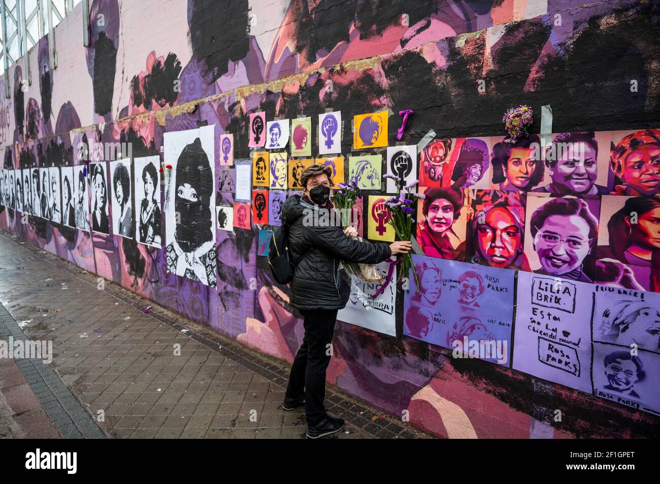 Madrid, Spain. 8th March, 2021. A woman placing flowers in a feminist mural that appeared today vandalized during International Women's Day. Placards of women have been placed over the paintings after the mural was vandalized with black paint. The mural represents famous women from around the world, with the faces of 15 women who are part of history for their fight in favor of equality: Angela Davis, Frida Kahlo, Nina Simone, Rigoberta Menchu, Lucia Sanchez Saornil, Rosa Arauzo, Valentina Tereshkova, Chimamanda Ngozi, Emma Goldman, Kanno Sugato, Liudmila Pavlichenko, Billy Jean King, Gata Catt Stock Photo