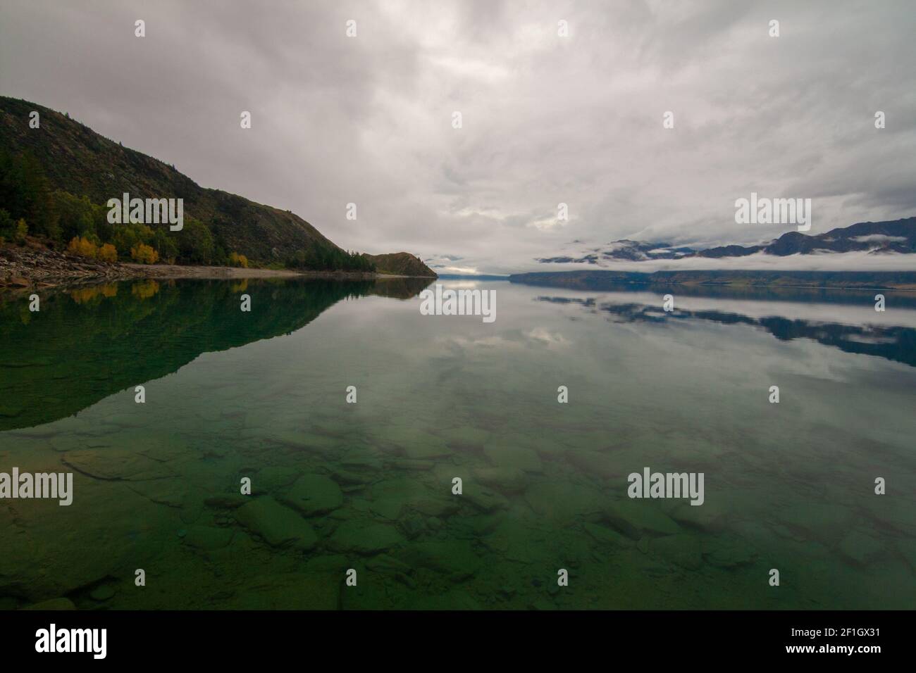 Pristine clear waters of Lake Hawea near Albert Town at autumn misty morning, Glacier valley, New Zealand Stock Photo