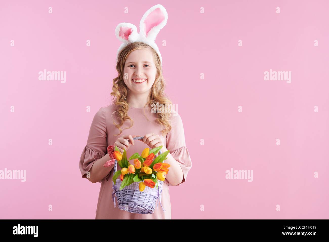 Portrait of happy modern girl in pink dress with bunny ears and easter basket isolated on pink. Stock Photo