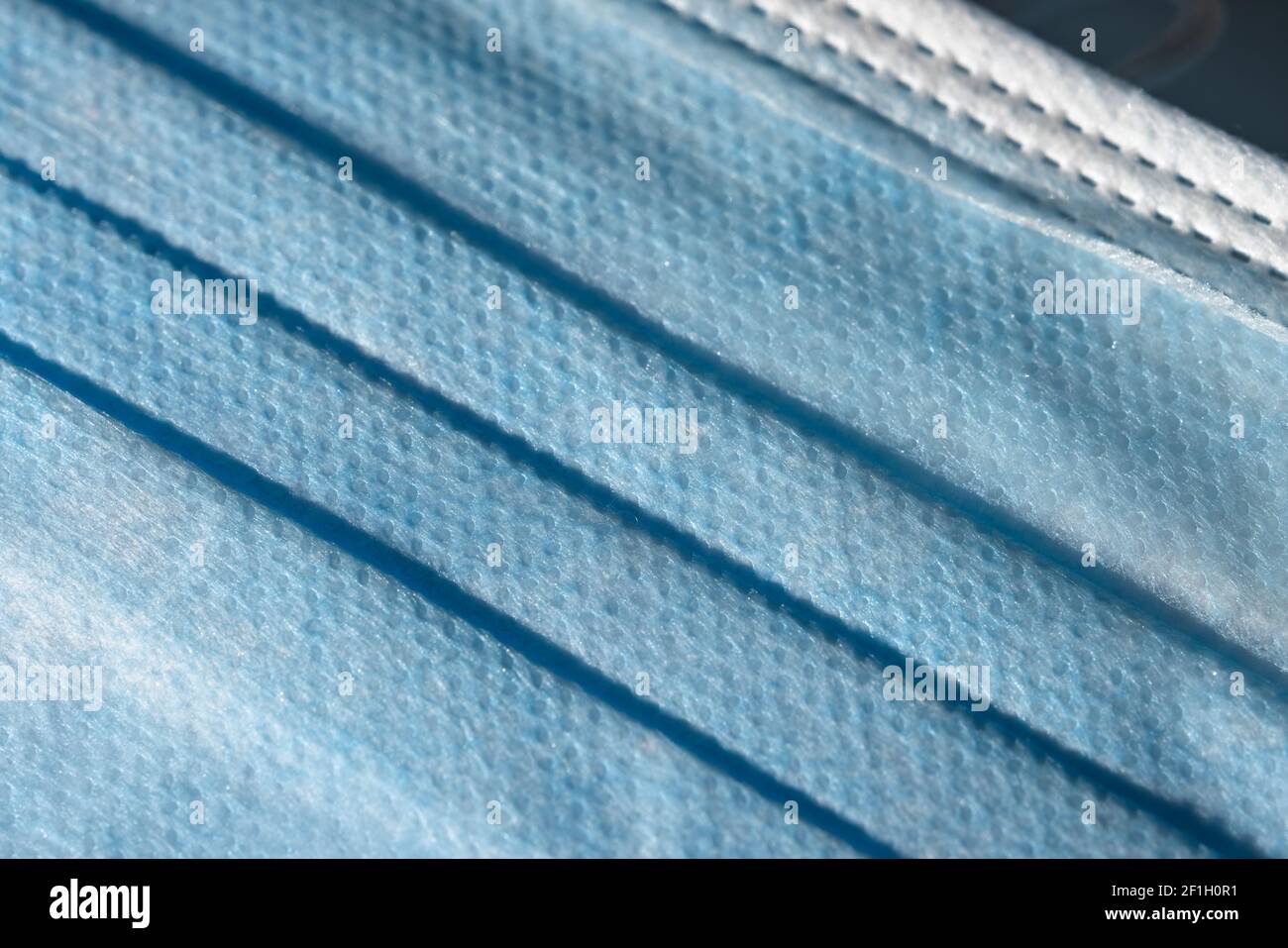 Close up of the front blue surface of a medical or surgical face mask. Man made single use item of Personal protective equipment, plastic texture. Stock Photo