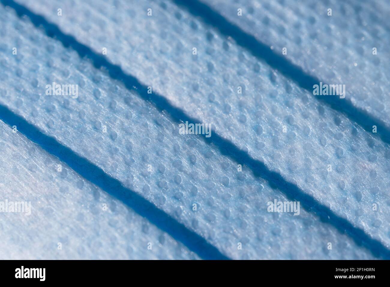 Blue doctors face mask used for coronavirus or covid forms a full frame background texture. Dimpled blue surface and microscopic fiber material detail Stock Photo