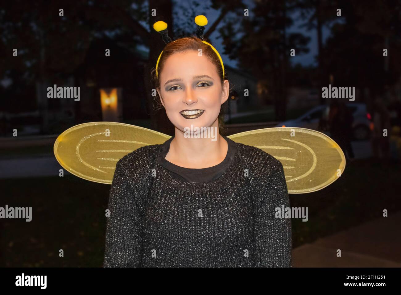 10-31-2018 Tulsa, USA Petty teenaged girl dressed as a bumble bee for Halloween with gold wings and sparkly lipstick out trick or treating at night Stock Photo