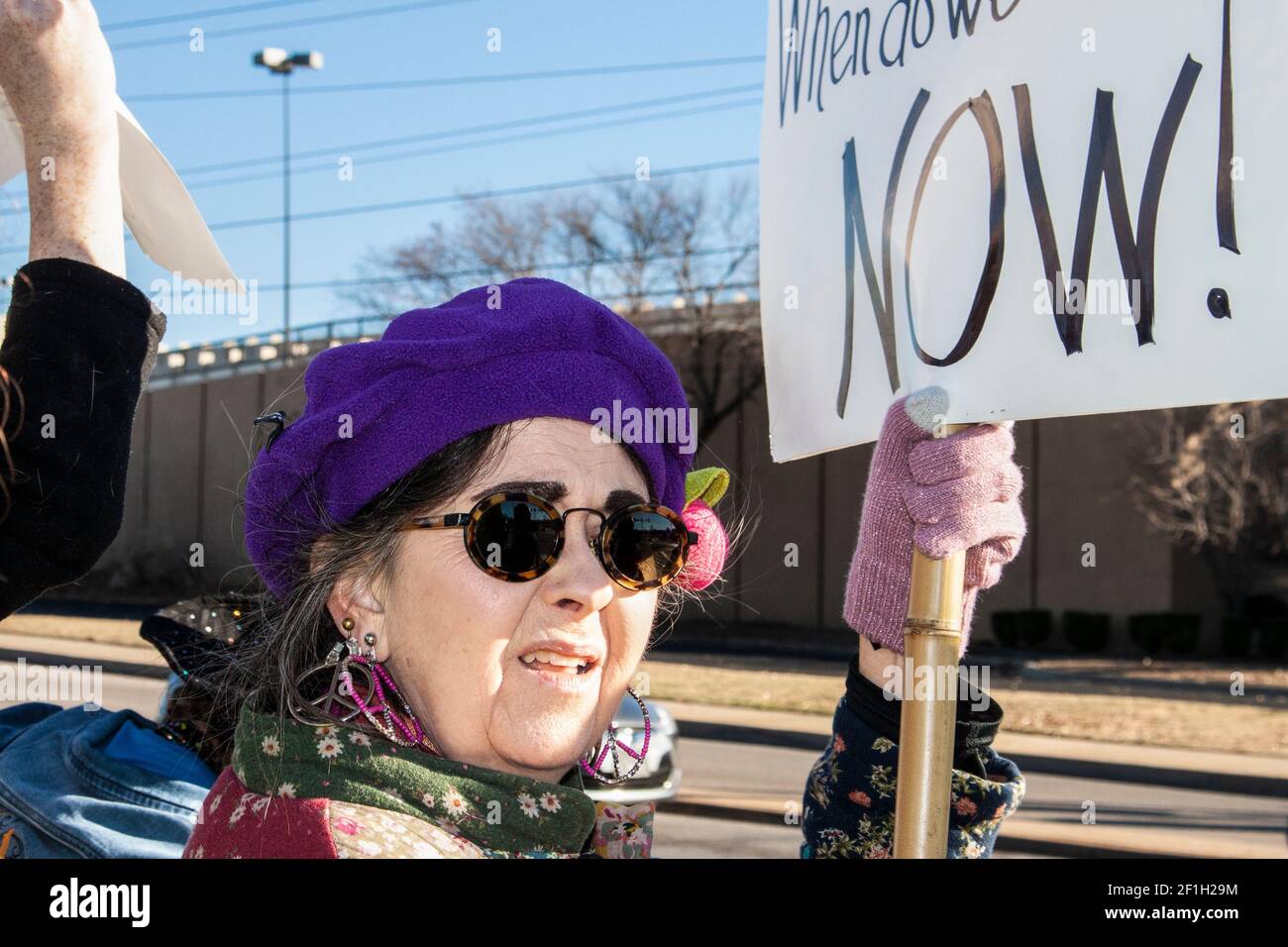 01-04-2020 Tulsa USA - Worried looking senior citizen woman with colorful clothing and peace earrings at war protest with sign Stock Photo