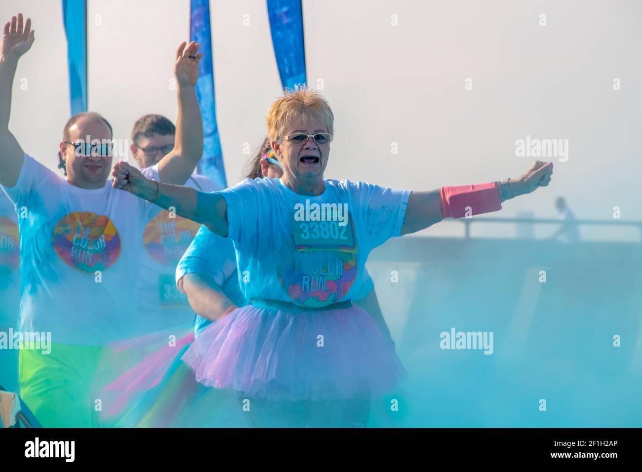 4 - 6 - 2019 -Tulsa USA Two runners - on a senior citizen woman in a tutu and a man behind her - hold their arms up as they run through colored powder Stock Photo