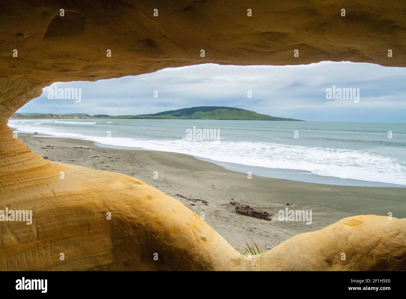 View from the cave in the cliff to the Gemstone beach and Pahia hill, natural window of old shelter in surreal shapes of cliffs caves, The Catlins in Stock Photo