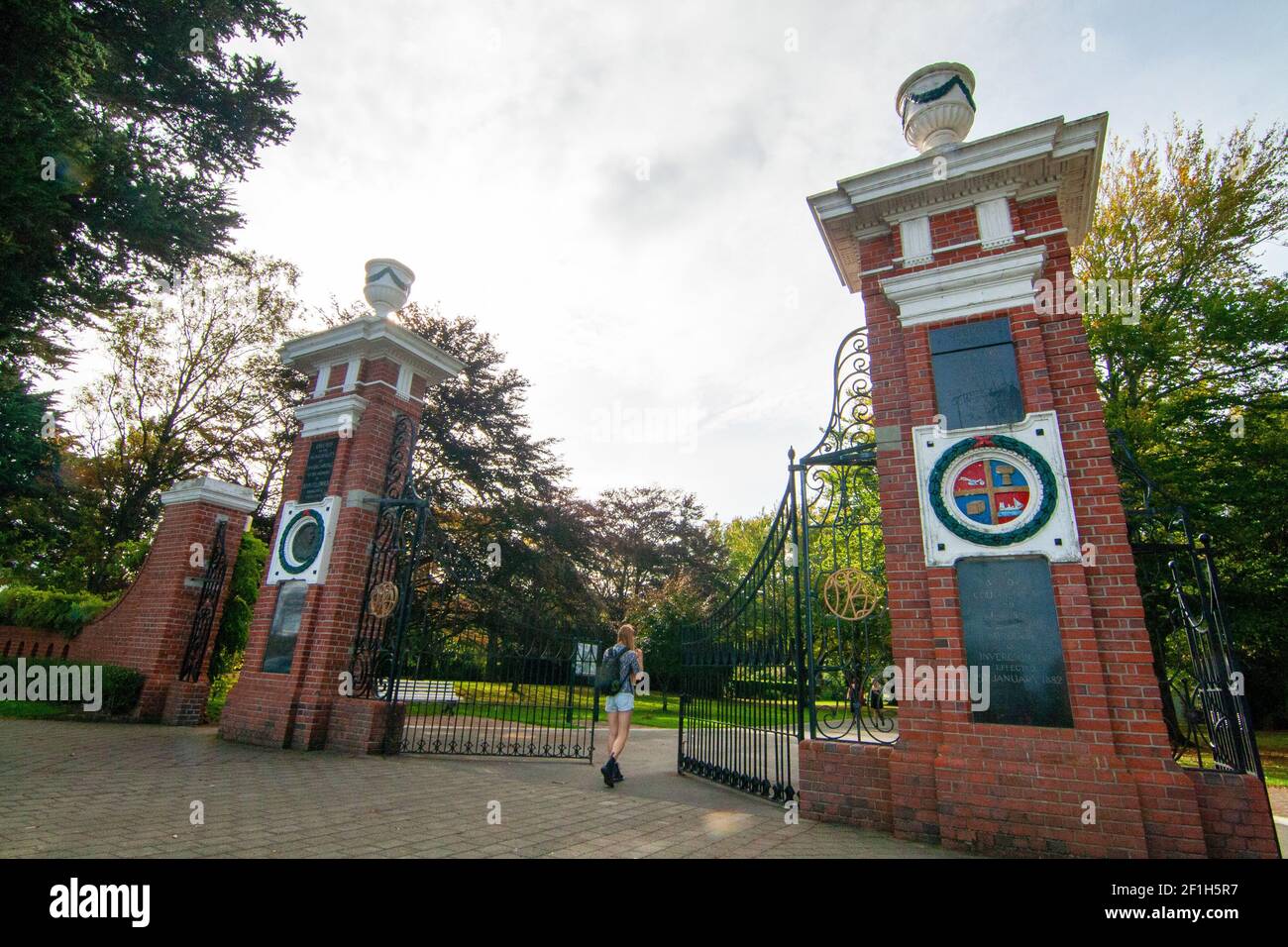 Female tourist with backpack walking into the main entrance of Queens Park in Invercargill, Feldwick Memorial Gates, Southland, New Zealand Stock Photo