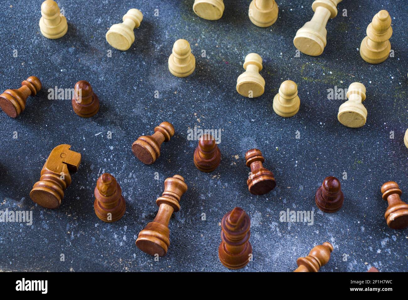 A closeup shot of partially standing and fallen wooden chess pieces from both sides on a blue surface Stock Photo