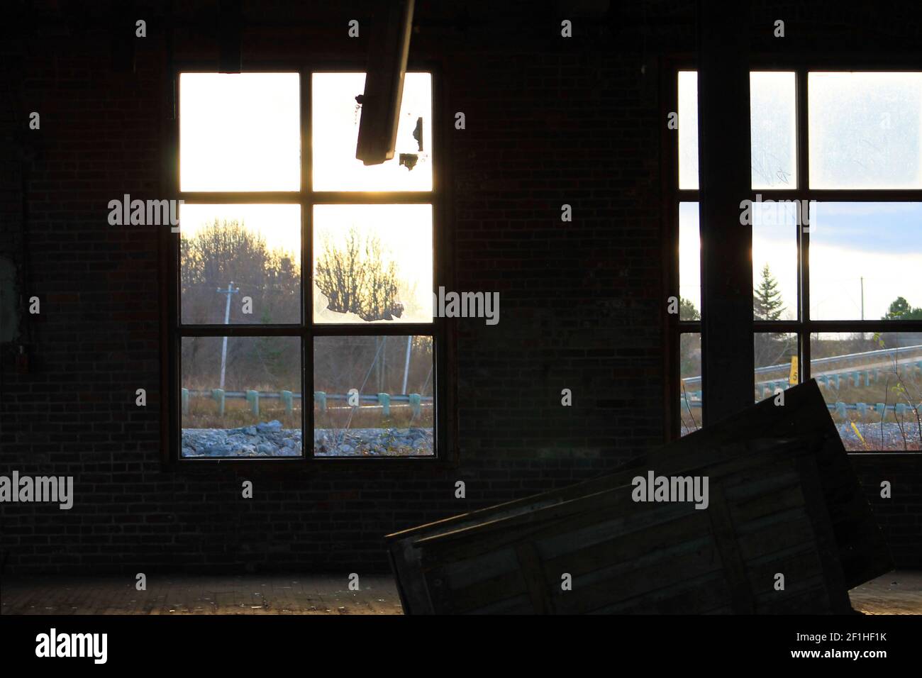 Interior view of an old, run-down, and abandoned factory building. Big, empty room with brick walls, exposed beams, and florescent light fixtures. Stock Photo