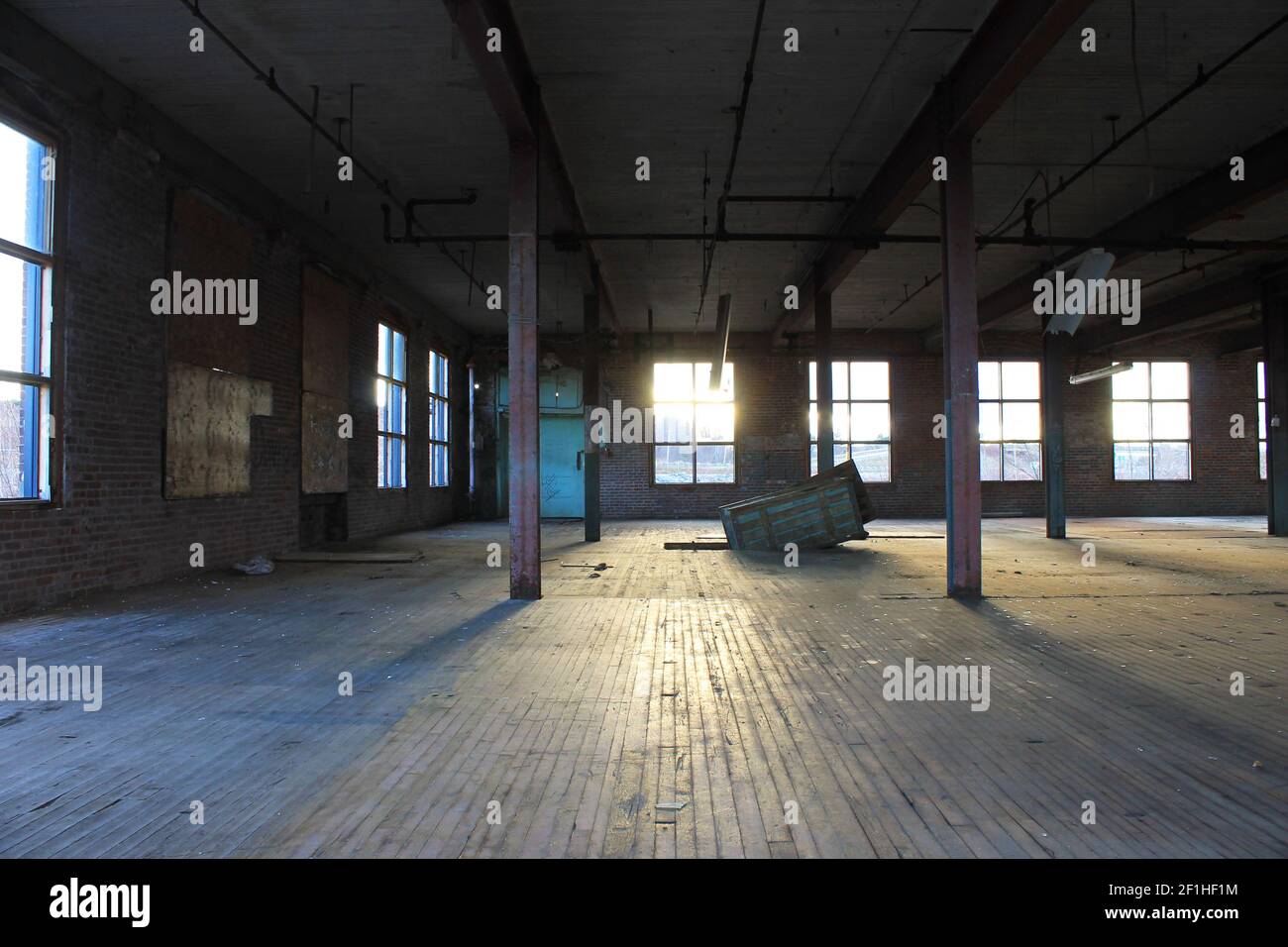 Interior view of an old, run-down, and abandoned factory building. Big, empty room with brick walls, exposed beams, and florescent light fixtures. Stock Photo