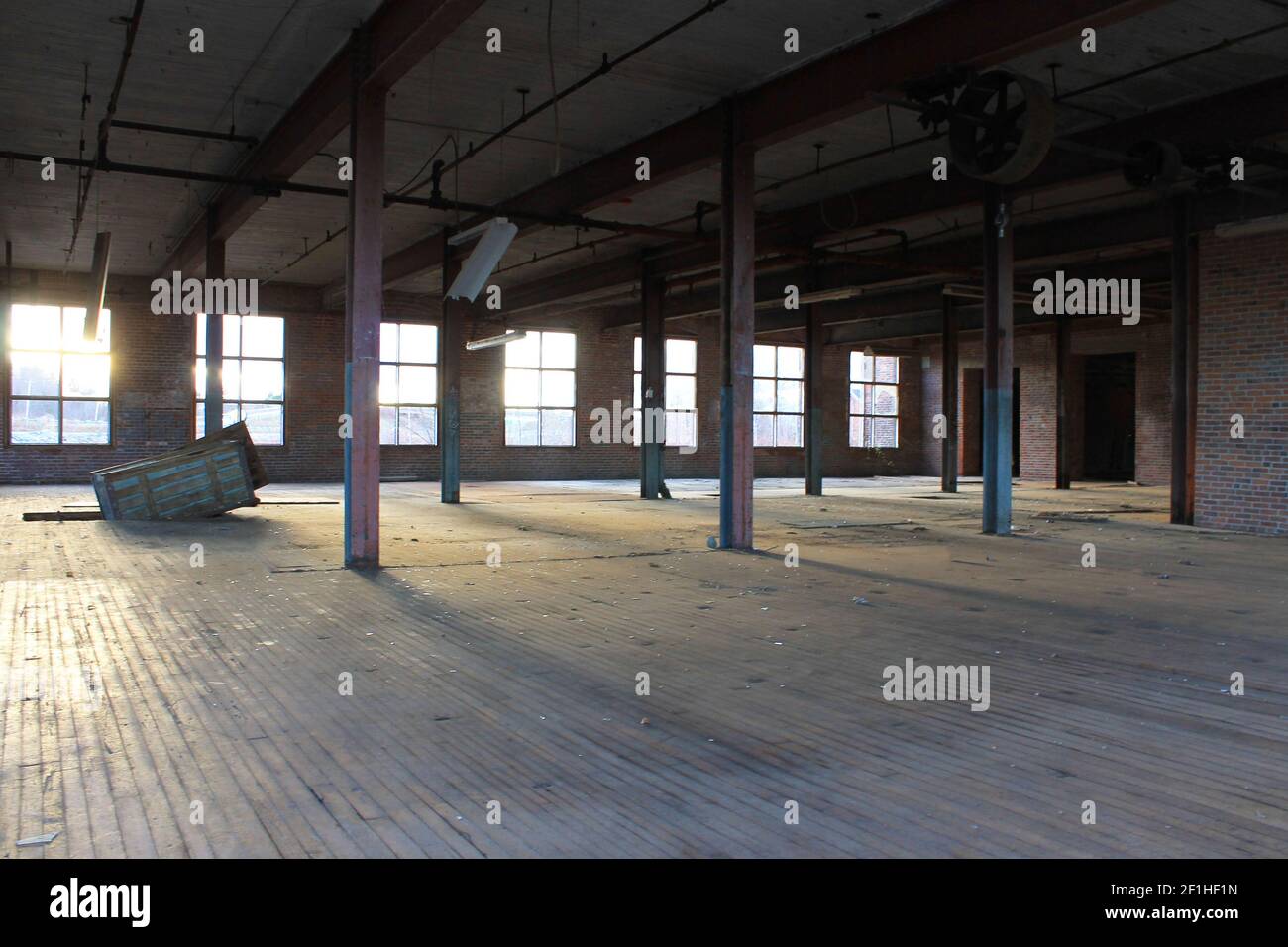Interior view of an old, run-down, and abandoned factory building. Big, empty room with brick walls, exposed beams, and florescent light fixtures. Stock Photo