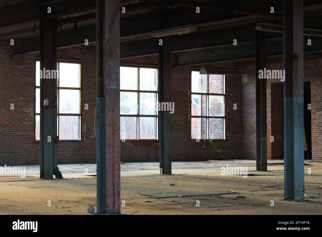 Interior view of an old, run-down, and abandoned factory building. Big, empty room with brick walls, exposed beams, and florescent light fixtures. Stock Photo