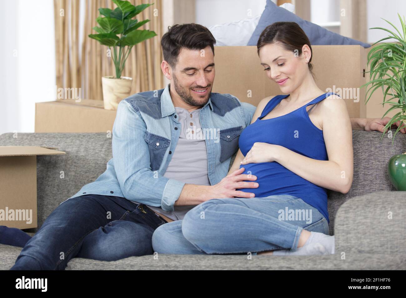 a man embracing happy pregnant woman sitting on couch Stock Photo Alamy