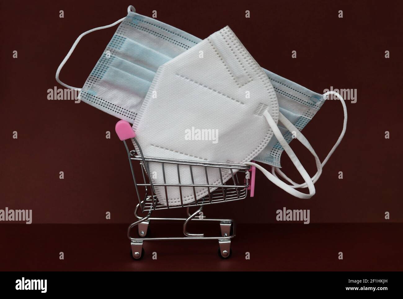 A FFP2 mask and a surgical mouth guard in a shopping cart against a brown background Stock Photo