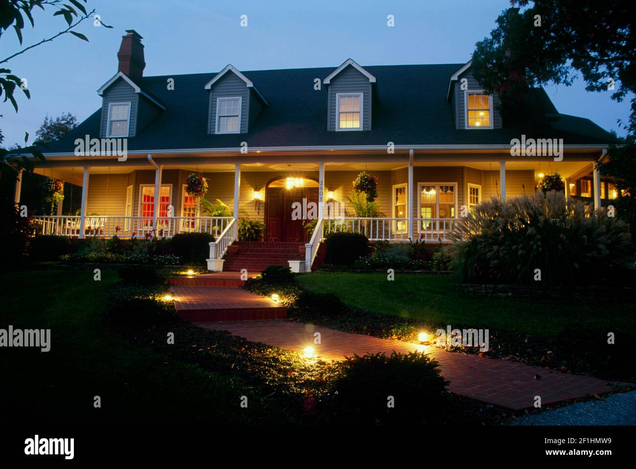 Cape cod style house lit for evening guest arriving for party by well lit walkways and welcoming views, Missouri Stock Photo