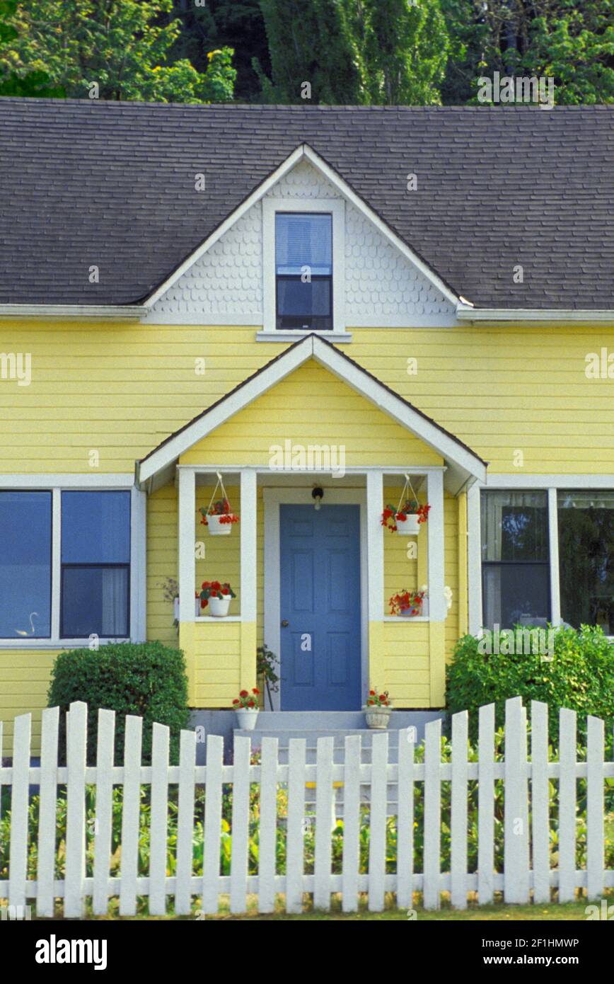 Yellow wooden clapboard house with picket fence and hanging geraniums, Oregon, USA Stock Photo