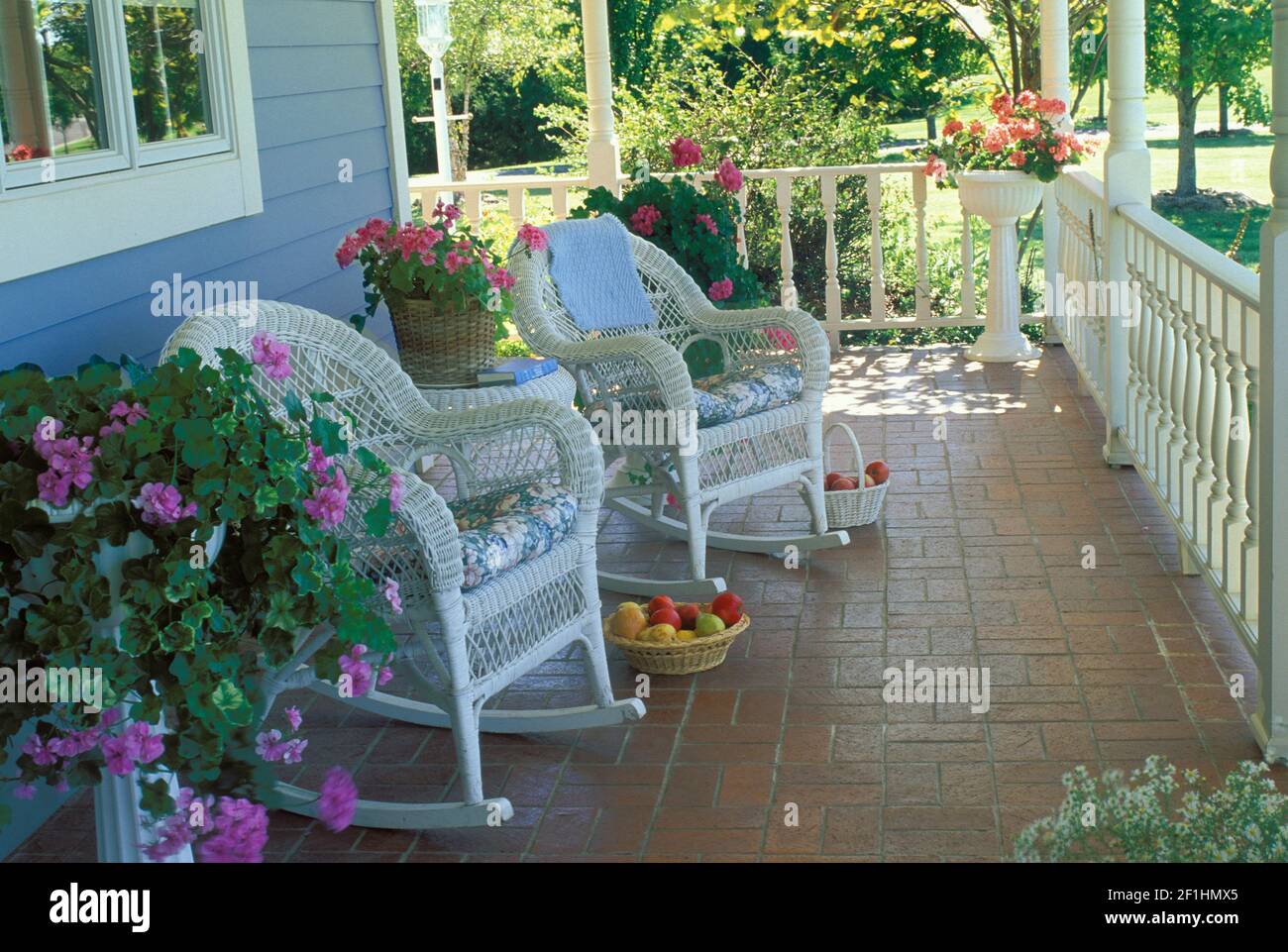 Wicker rocking chairs on a brick patio front porch with blooming potted flowers - a private place, Missouri, USA Stock Photo
