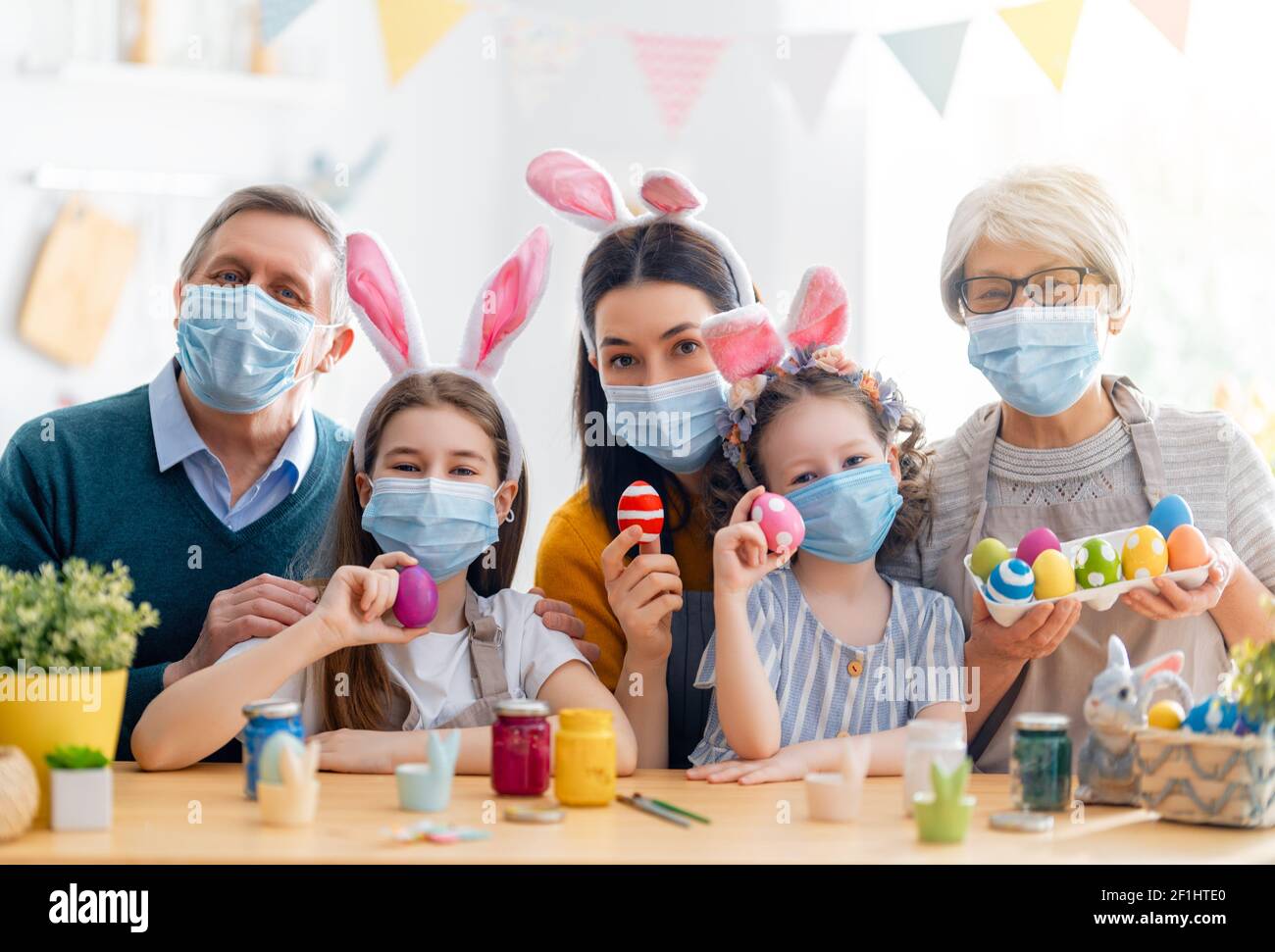 Mother, grandparents and children are painting eggs. Happy family are preparing for Easter. Cute little girls wearing bunny ears. Stock Photo