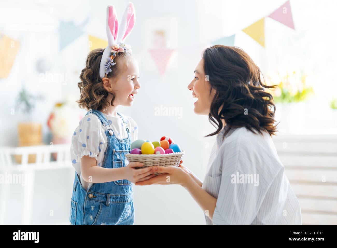 Happy holiday! Mother and her daughter with painting eggs. Family celebrating Easter. Cute little child girl is wearing bunny ears. Stock Photo