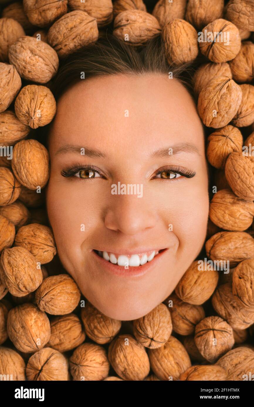 Woman smiling face on a walnuts background. Eating nuts. Strong teeth Stock Photo