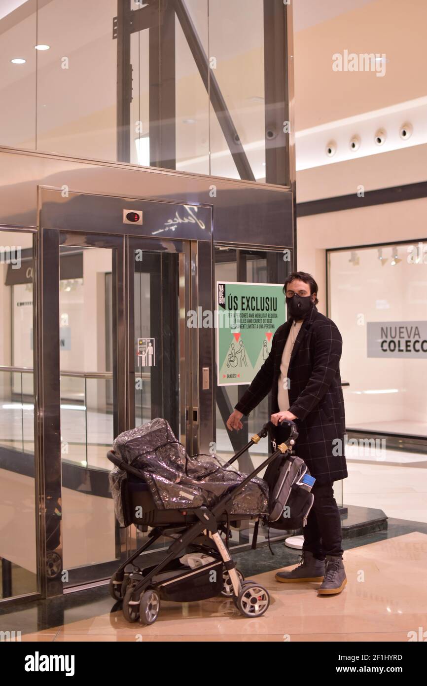 Man waiting the elevator with baby. Single dad protected with face mask and carrying a baby stroller protected with a plastic. Father with daughter. Stock Photo