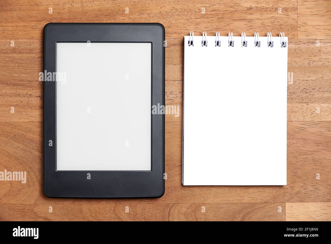 Electronic reader with blank screen and open notepad on a wooden ...