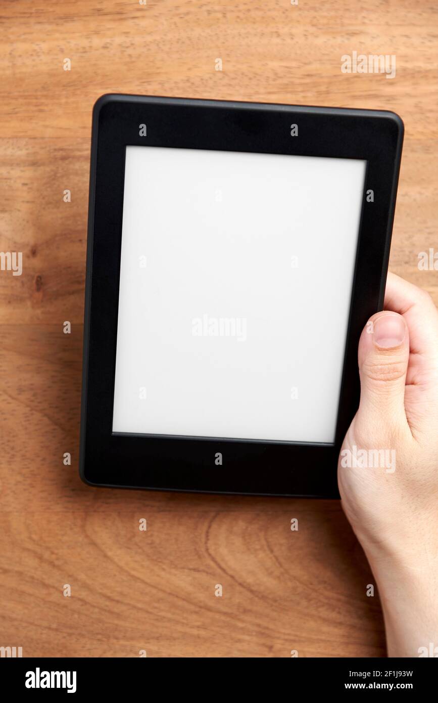 Young hand holding an electronic reader with blank screen on a wooden