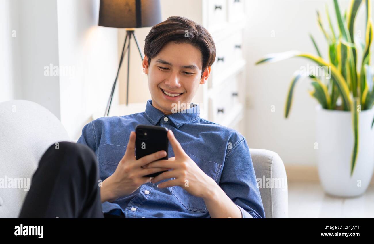 Young Asian man lying on sofa and using phone Stock Photo