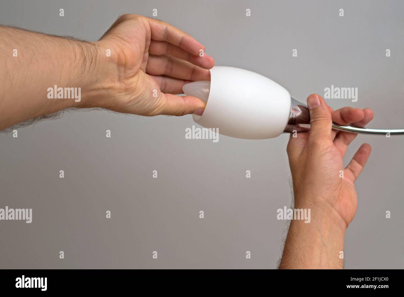 The left man's hand holds the arm of the chandelier the right hand screws or unscrews energy-saving candle-type lamp on white ceiling background. Conc Stock Photo