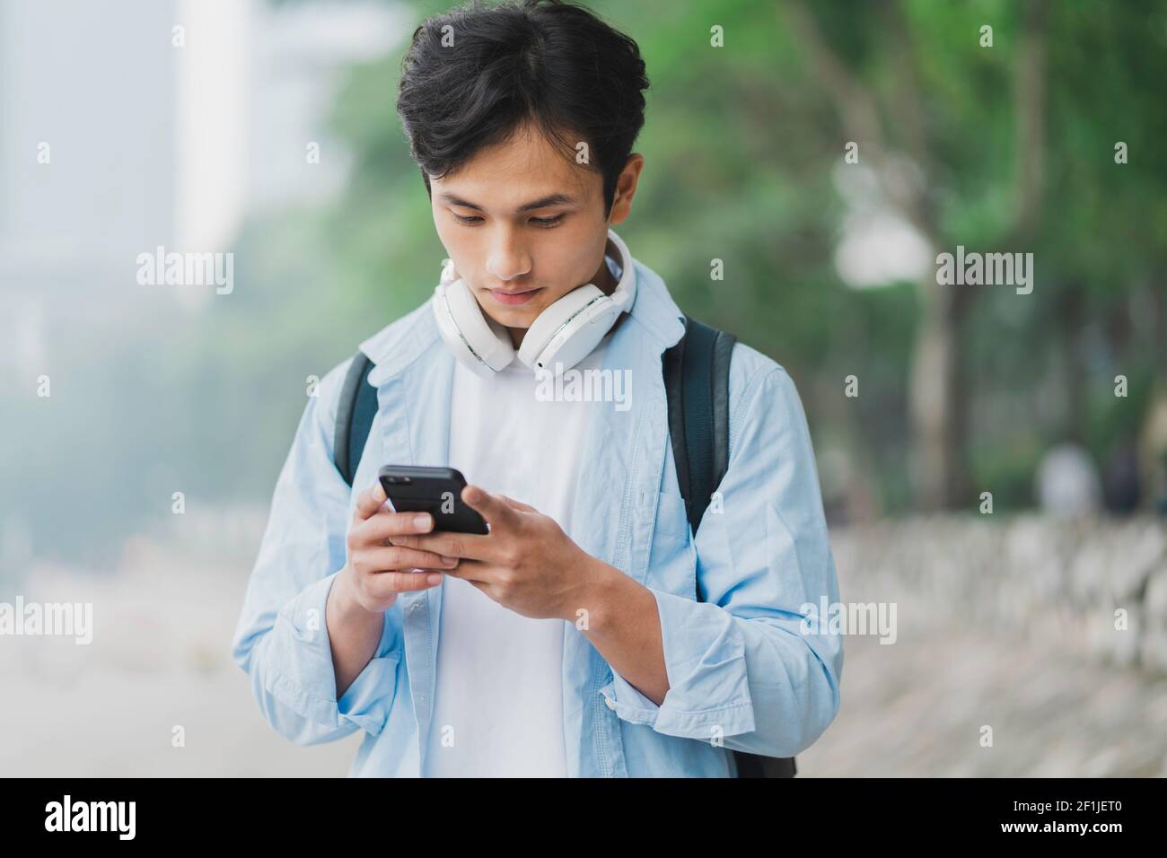 Young Asian man wearing backpack and looking at phone screen Stock Photo