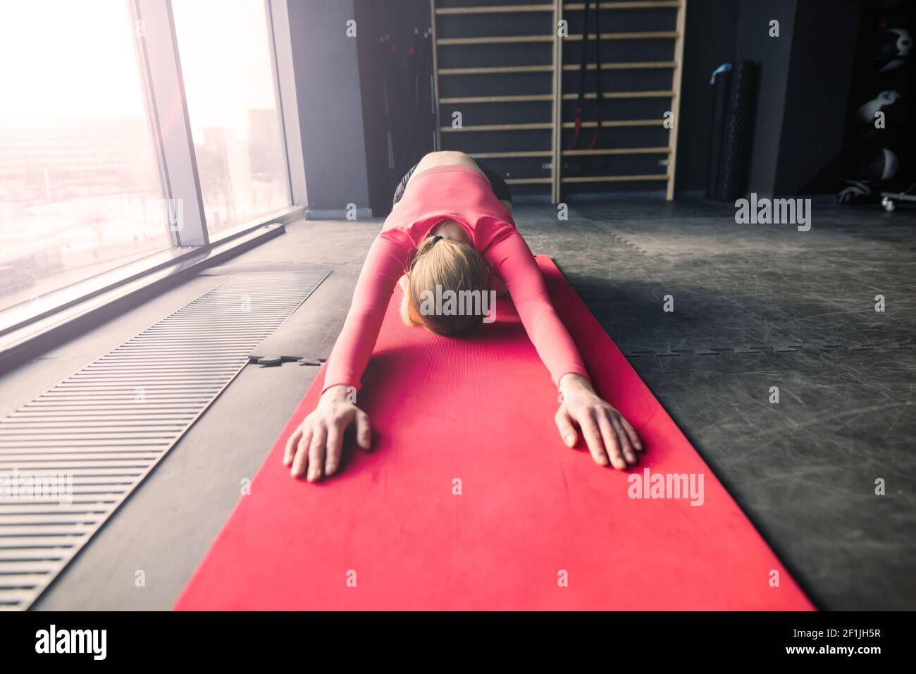 Woman practicing advanced yoga on mat against a large window Stock Photo