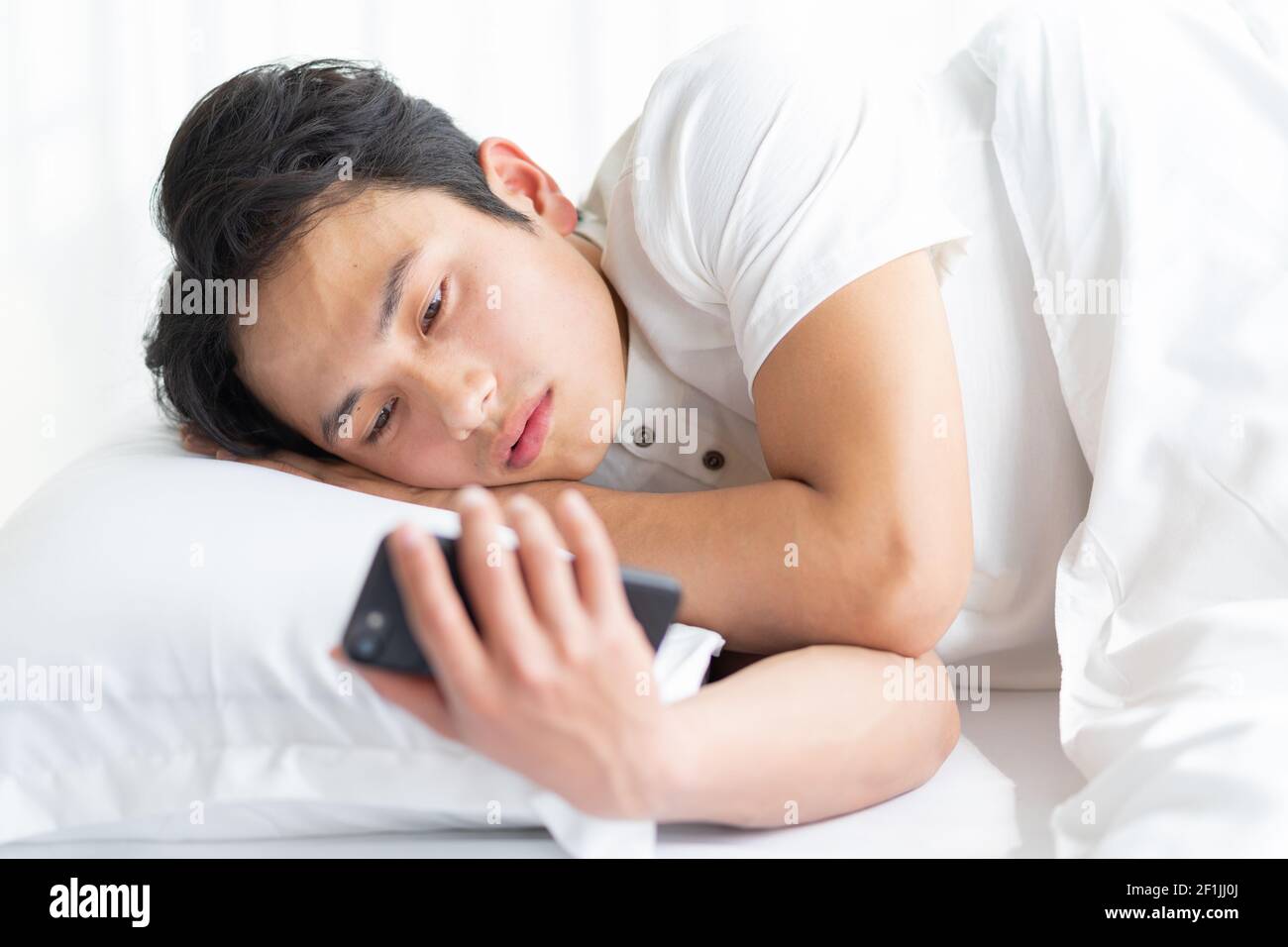 Young man lying in bed using a phone Stock Photo