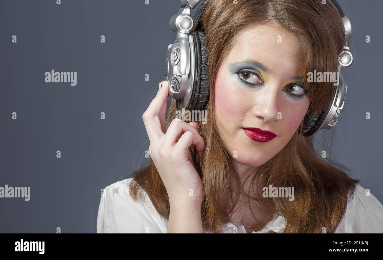 Teenager, redhead girl with helmet on her head listening to music on a flat gray background Stock Photo