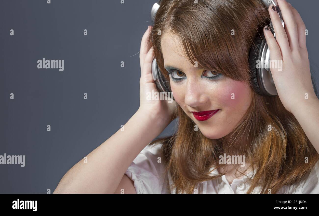 Entertainment redhead girl with helmet on her head listening to music on a flat gray background Stock Photo