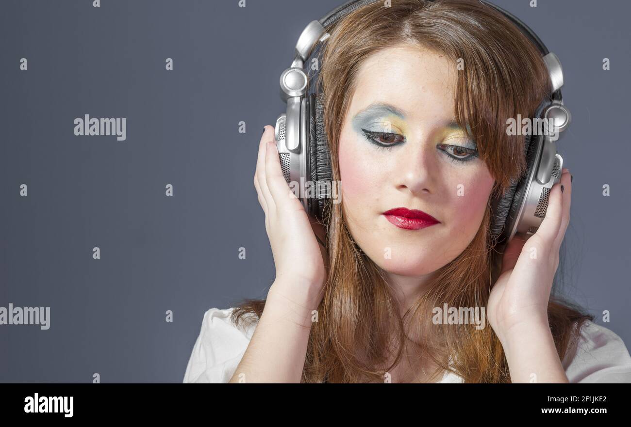 Teen redhead girl with helmet on her head listening to music on a flat gray background Stock Photo