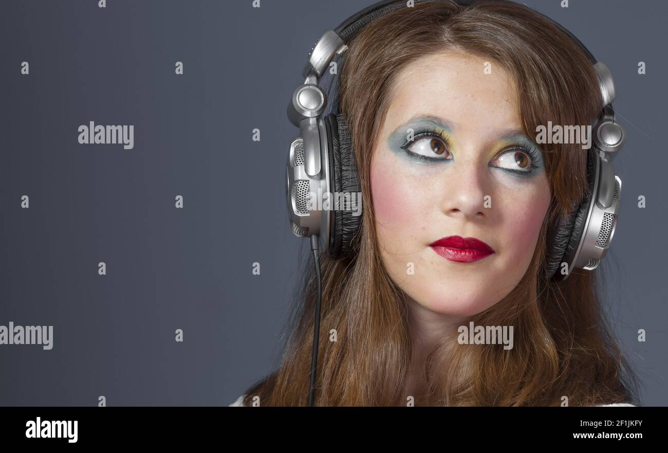 Redhead girl with helmet on her head listening to music on a flat gray background Stock Photo