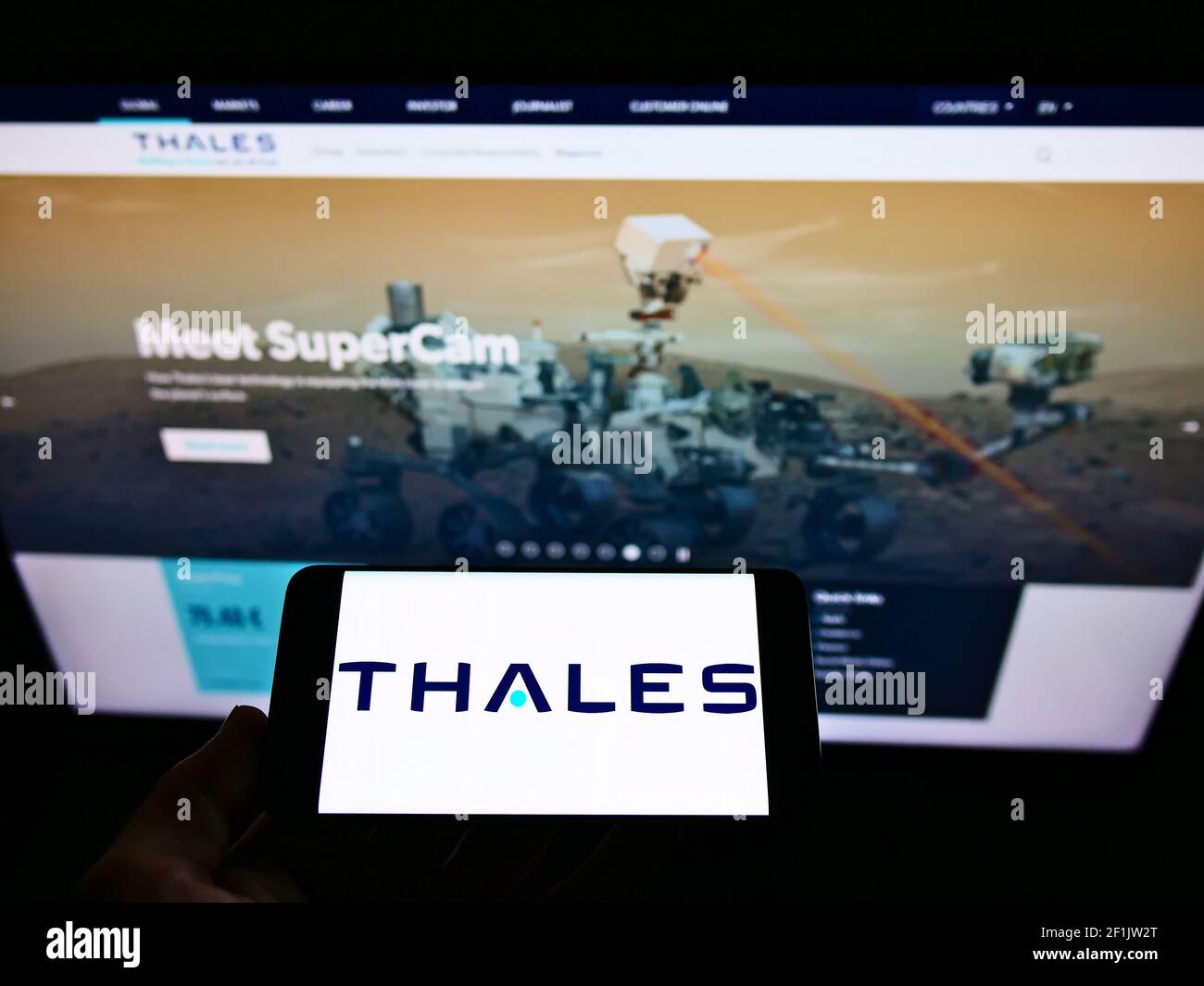 Person holding mobile phone with business logo of French defence company Thales SA on screen in front of website. Focus on phone display. Stock Photo