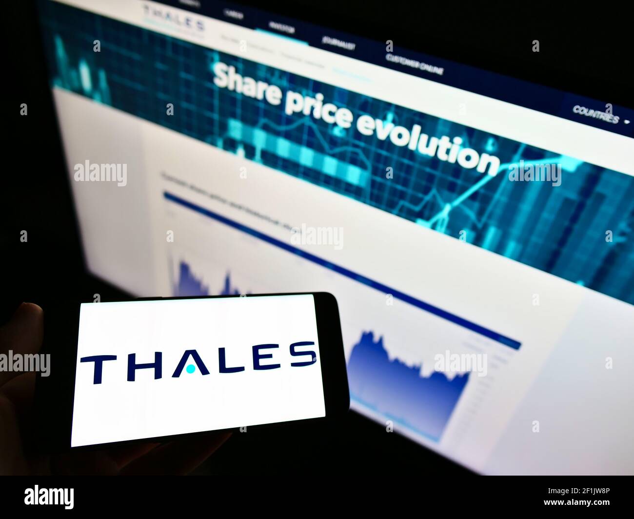 Person holding mobile phone with business logo of French defence company Thales S.A. on screen in front of website. Focus on phone display. Stock Photo