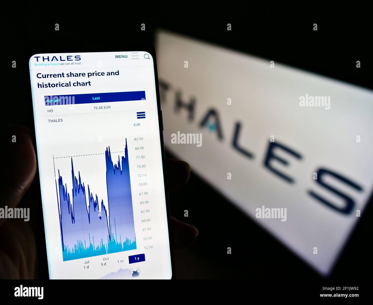 Person holding cellphone with web page and stock chart of French defence company Thales SA on screen with logo. Focus on center of phone display. Stock Photo