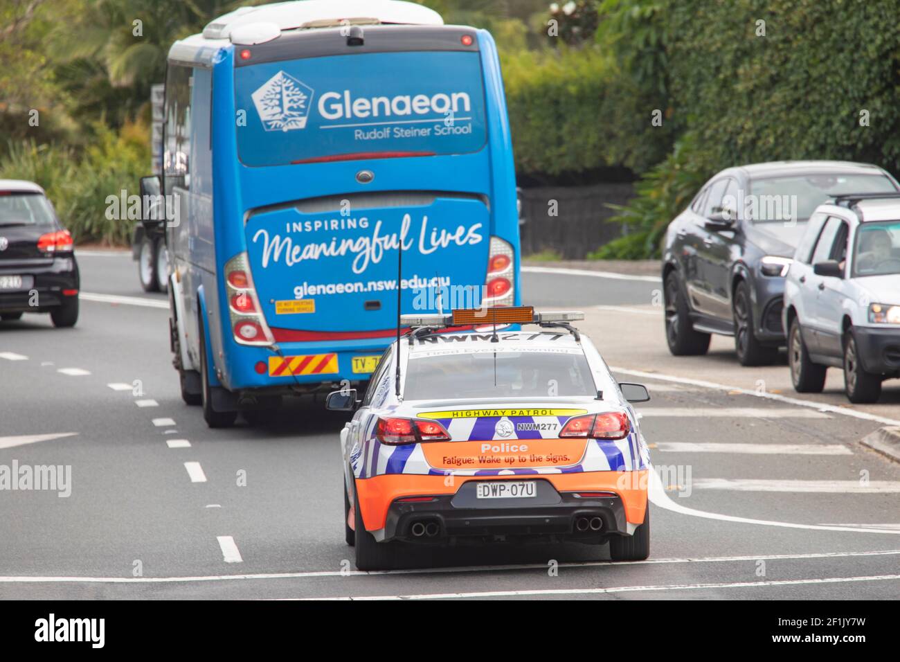Sydney police car, holden commodore, travelling behind Rudolf Steiner private school bus in North Sydney,NSW,Australia Stock Photo