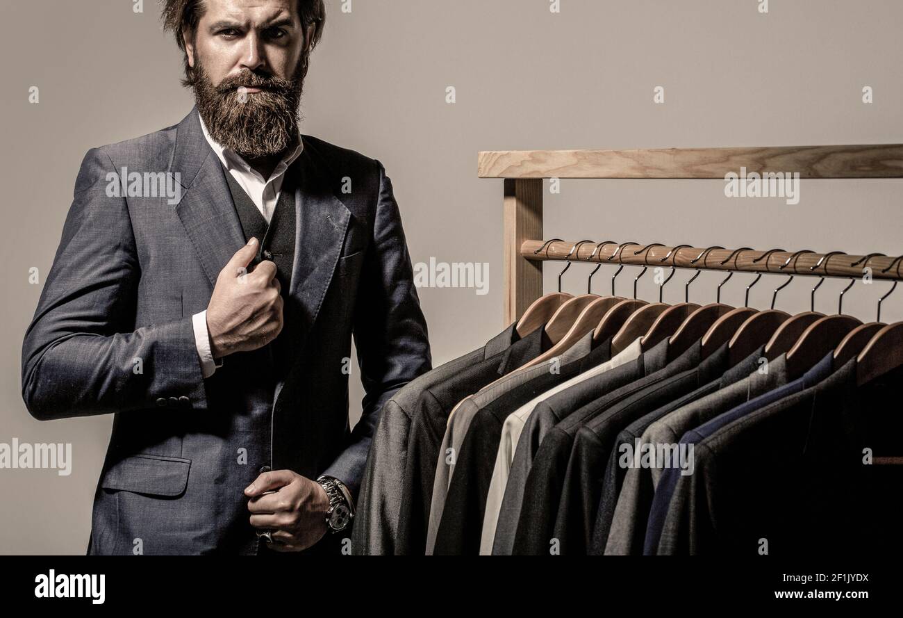 Male suits hanging in a row. Men clothing, boutiques. Tailor, tailoring. Stylish men's suit. Man suit, tailor in his workshop. Handsome bearded Stock Photo