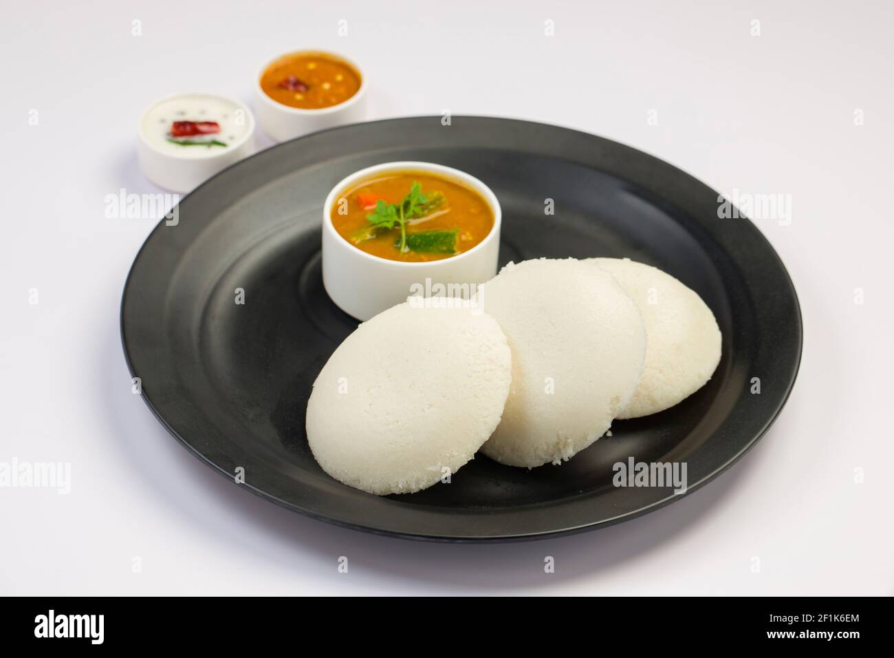 Idly or Idli, south indian main breakfast item which is beautifully arranged in a black plate on white background. Stock Photo