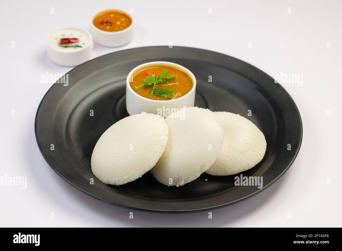 Idly or Idli, south indian main breakfast item which is beautifully arranged in a black plate on white background. Stock Photo