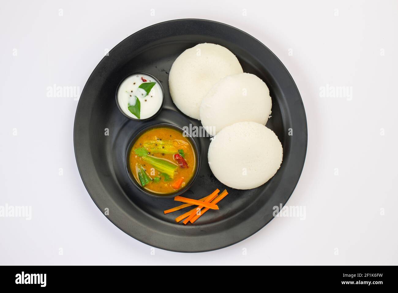 Idly or Idli, south indian main breakfast item which is beautifully arranged in a black plate on white background. Stock Photo