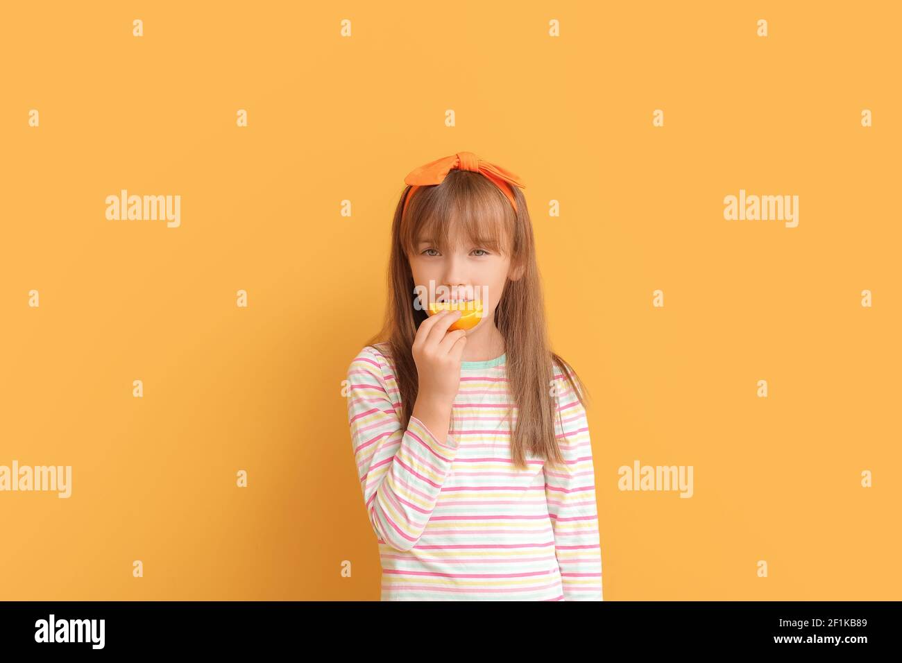 Cute little girl eating orange on color background Stock Photo - Alamy