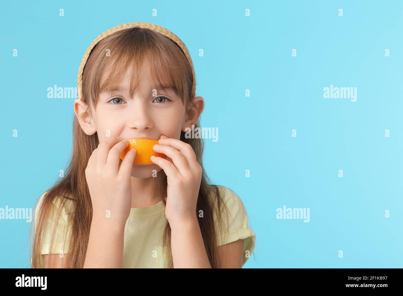 Cute little girl eating orange on color background Stock Photo - Alamy
